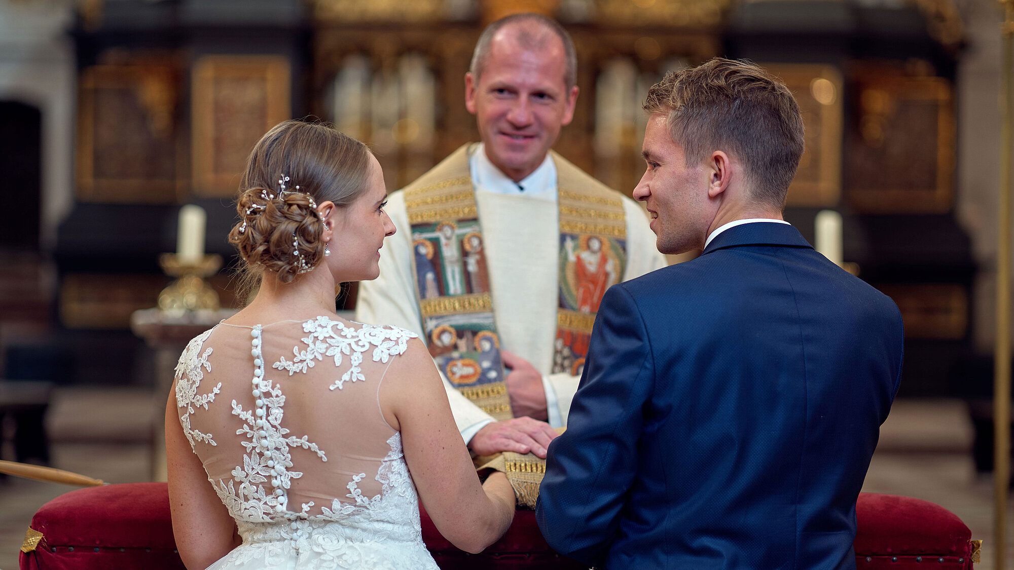 Ein junges Brautpaar erhält bei der kirchlichen Trauung den priesterlichen Segen von Dekan Roman Gerl und schaut sich dabei an.