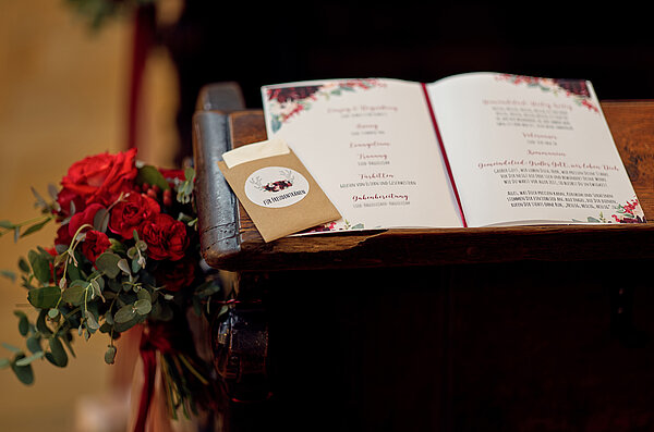 Nahaufnahme auf das Programmheft einer kirchlichen Hochzeit, das auf einer Kirchenbank liegt.
