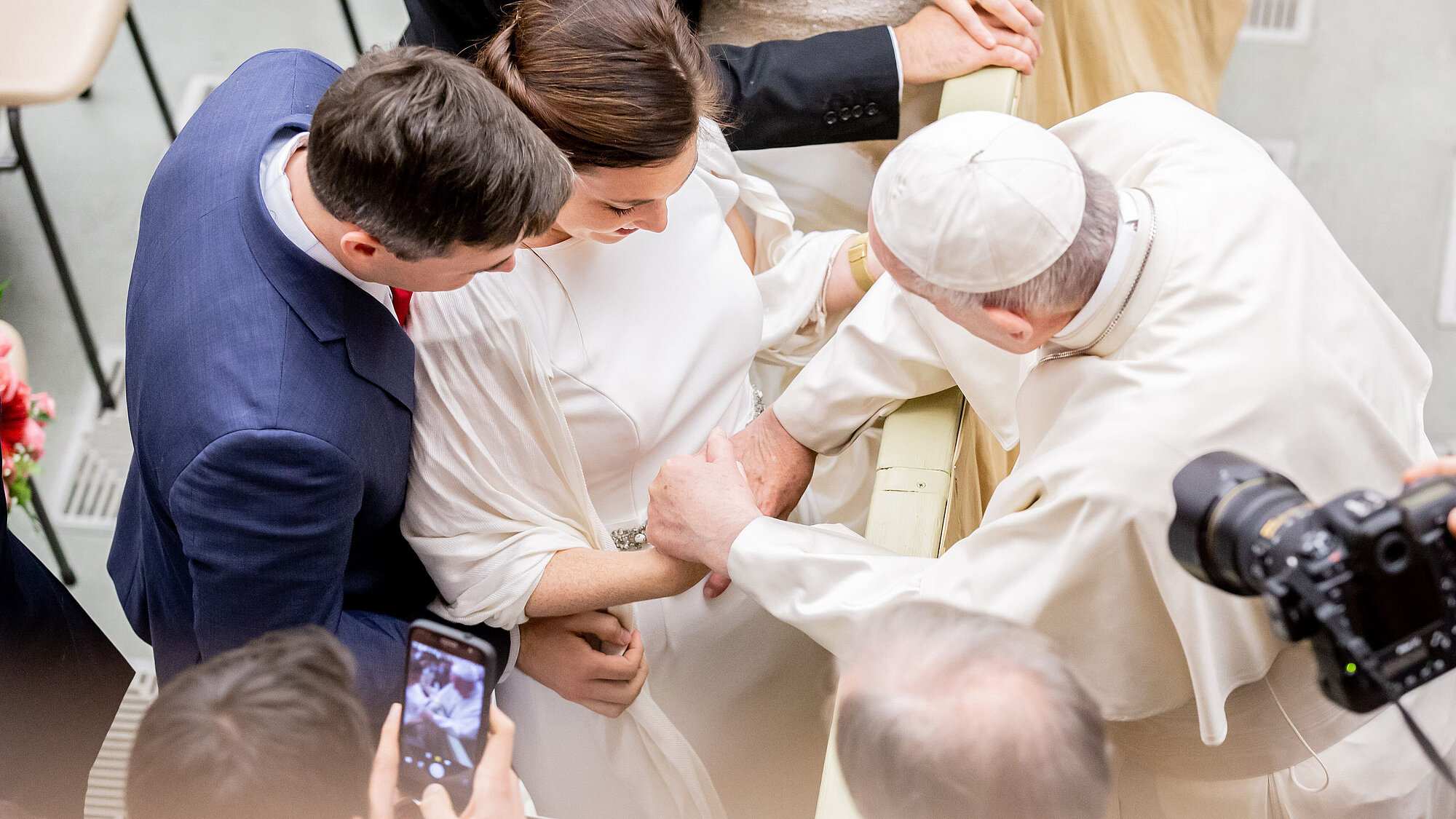 Blick von oben auf ein junges, frisch vermähltes Paar, das den Segen von Papst Franziskus erhält.