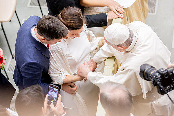 Blick von oben auf ein junges, frisch vermähltes Paar, das den Segen von Papst Franziskus erhält.