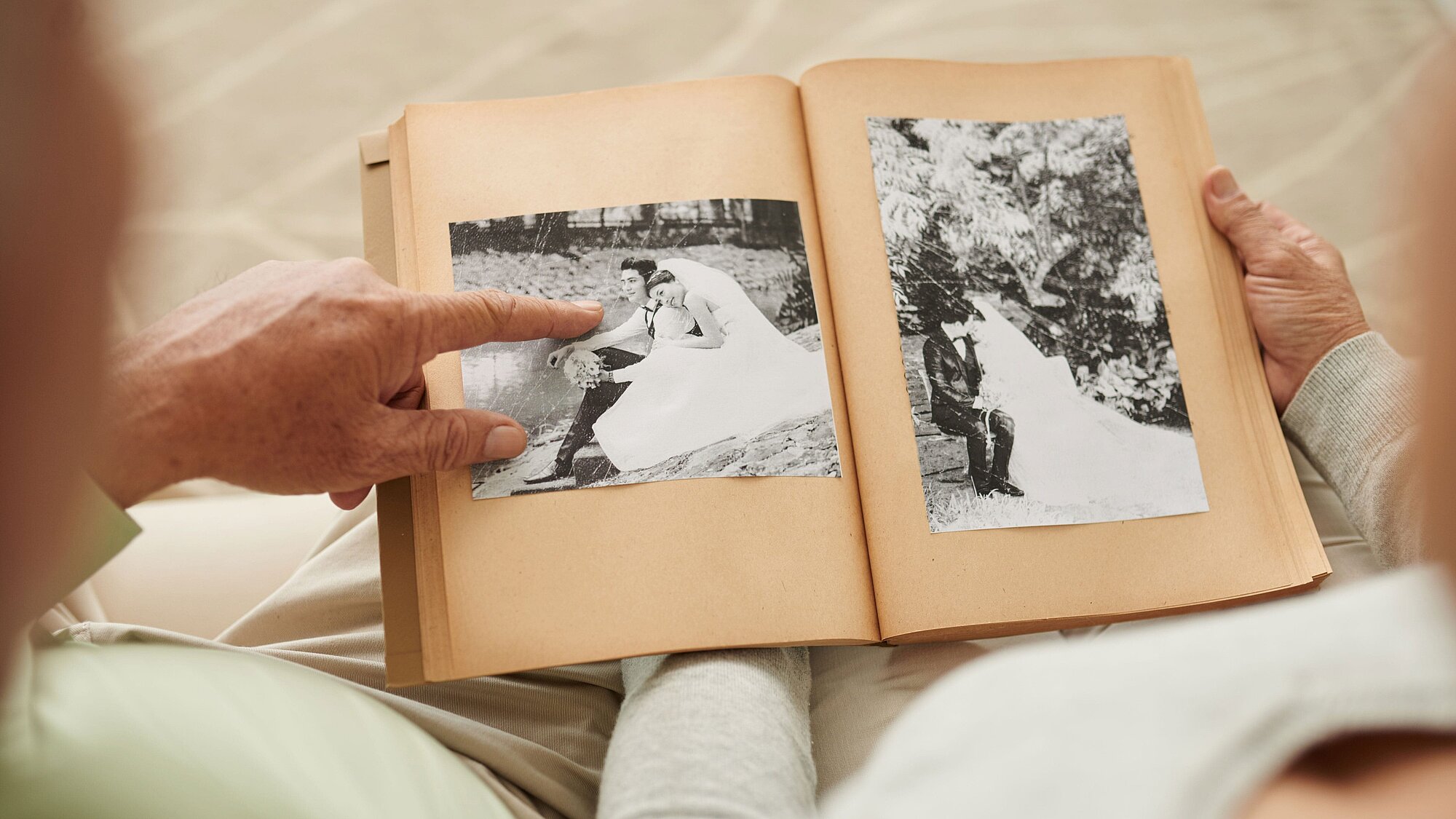 Blick über die Schultern eines älteren Paares, das sich alte Fotos ihrer kirchlichen Trauung ansieht.