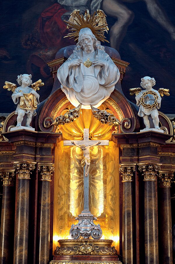 Eine Jesusfigur einer Kirche, die von zwei kleinen Engeln rechts und links begleitet wird.